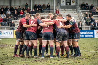 Joueurs de rugby amateurs en huddle avant un match de Fédérale 3, jerseys colorés sur terrain boueux