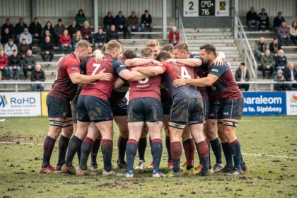 Joueurs de rugby amateurs en huddle avant un match de Fédérale 3, jerseys colorés sur terrain boueux